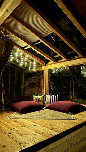 A cozy room with a wooden floor, a bed with two pillows, a window with string lights, and a view of trees outside. - SUMDA KONAKLAR (Camlihemsin)