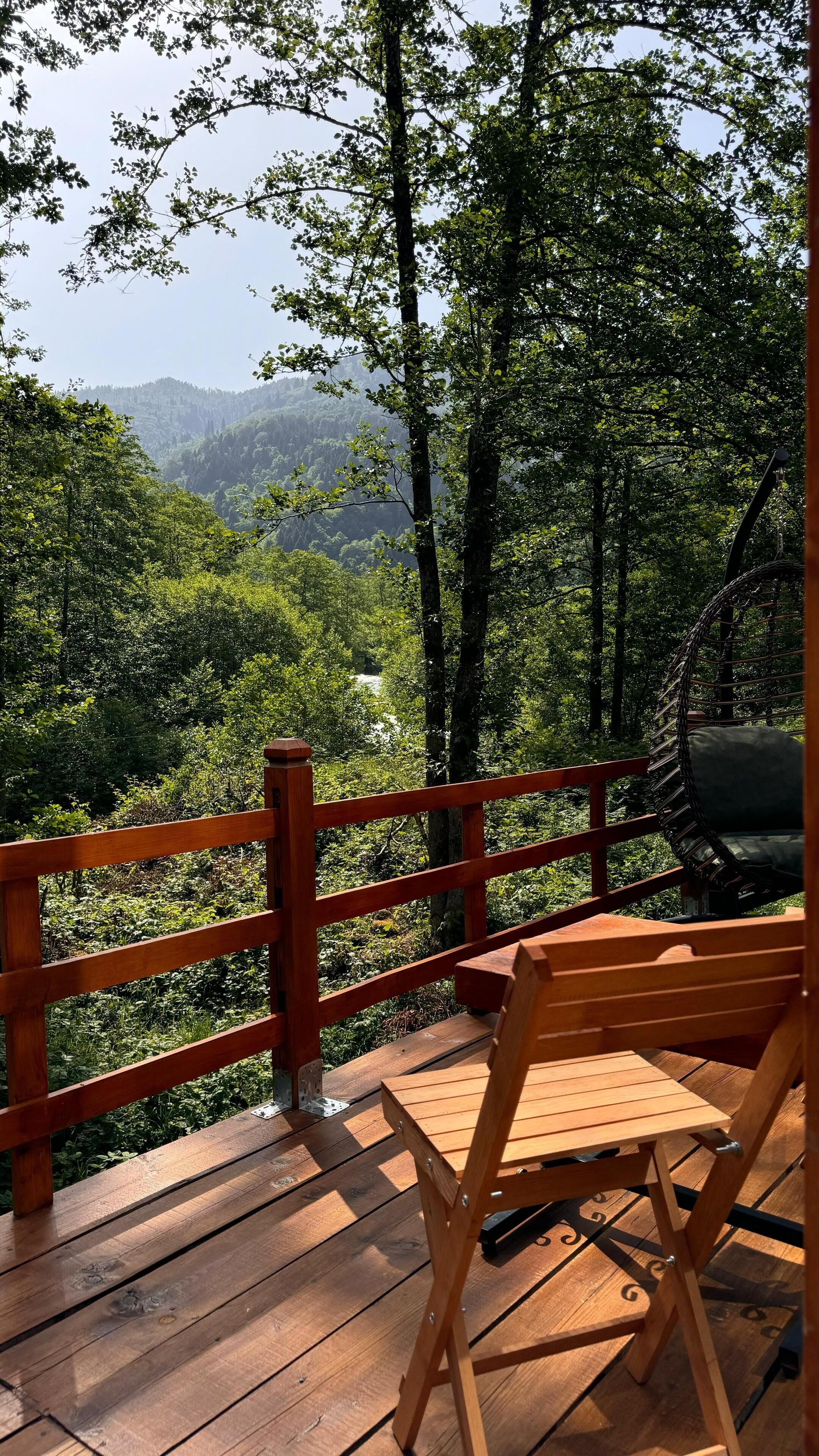 Eine Holzterrasse mit Stuhl und Schaukel mit Blick auf ein bewaldetes Tal und einen Fluss.