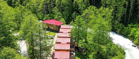 A row of cabins with red roofs nestled in a forested valley, surrounded by dense greenery and a river.