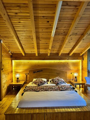Une chambre à coucher de style cabane en bois, avec un lit, deux lampes de chevet et une tête de lit portant l’inscription « SUMDA ».