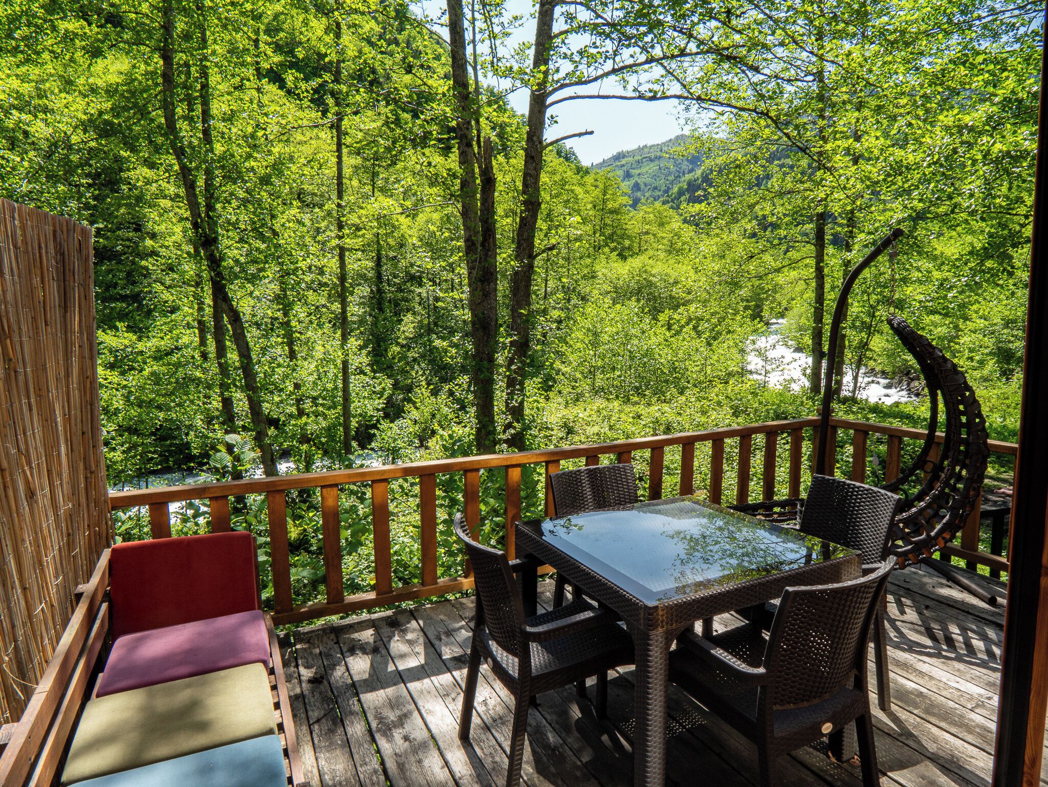 Eine Holzterrasse mit Tisch und Stühlen, umgeben von üppigem Grün und einer Bergkulisse.