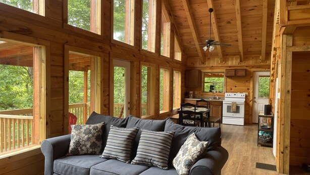 A cozy cabin interior with a grey sofa, wooden walls, large windows, a kitchen area, and a ceiling fan. - Luxury cabin with a "mountain  view" a hot tub, pet friendly and internet (Slade)