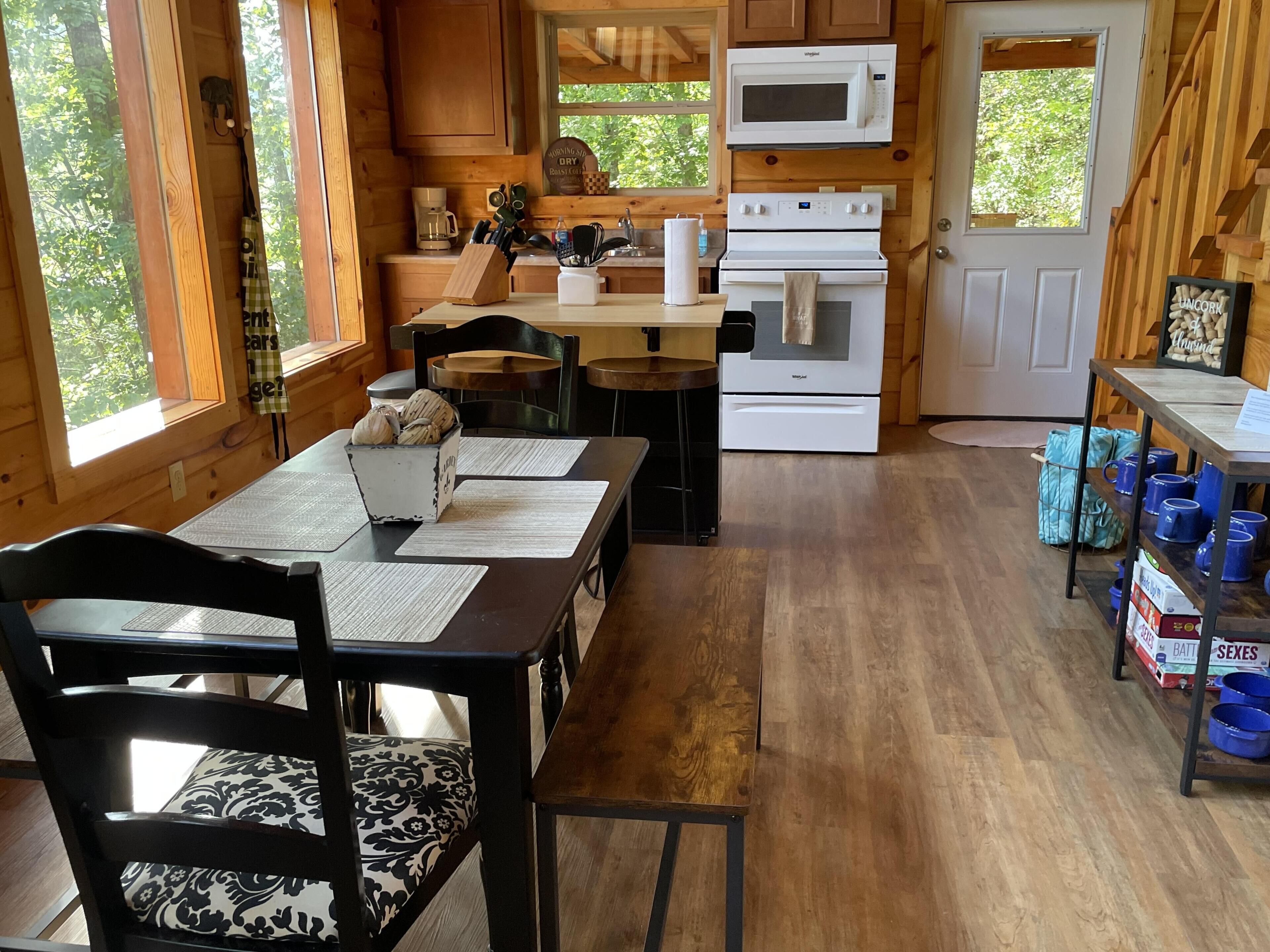 A wooden cabin kitchen with a dining area, wooden cabinets, a microwave, stove, and a view of the outdoors.