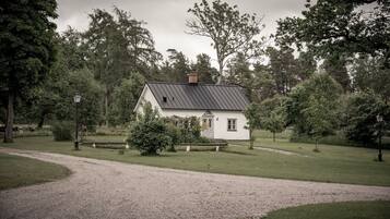 A white house with a dark roof, surrounded by a gravel path and lush greenery.