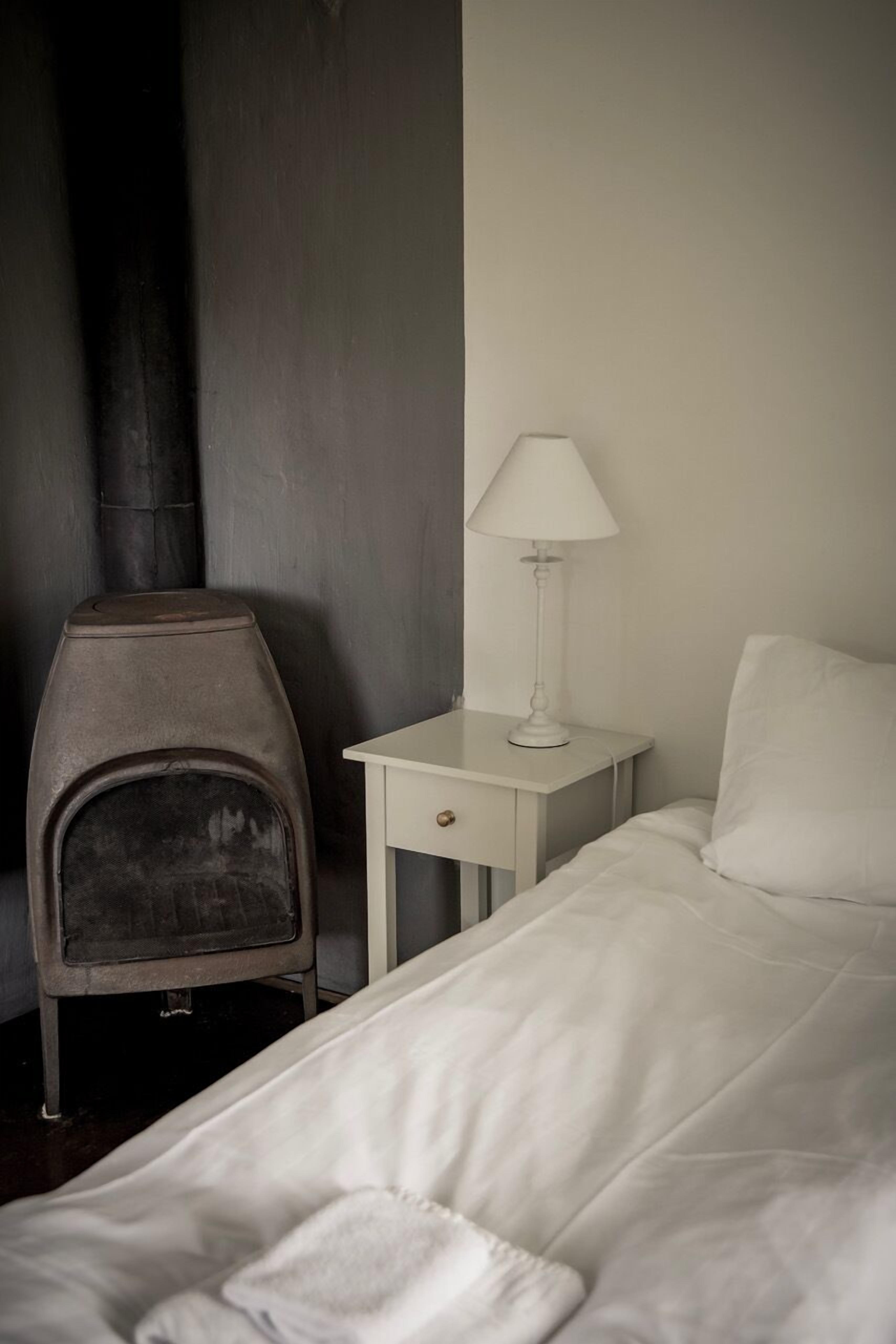 Un dormitorio con una cama, una mesita de noche con lámpara y un calentador.