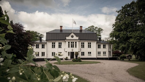 A large, white building with a symmetrical facade, multiple windows, and a flag on top. - Ruders Egendom (Tibro)