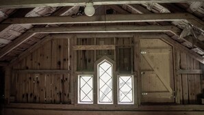 A rustic wooden barn interior with a sloped ceiling, wooden beams, and a large door. - Ruders Egendom (Tibro)