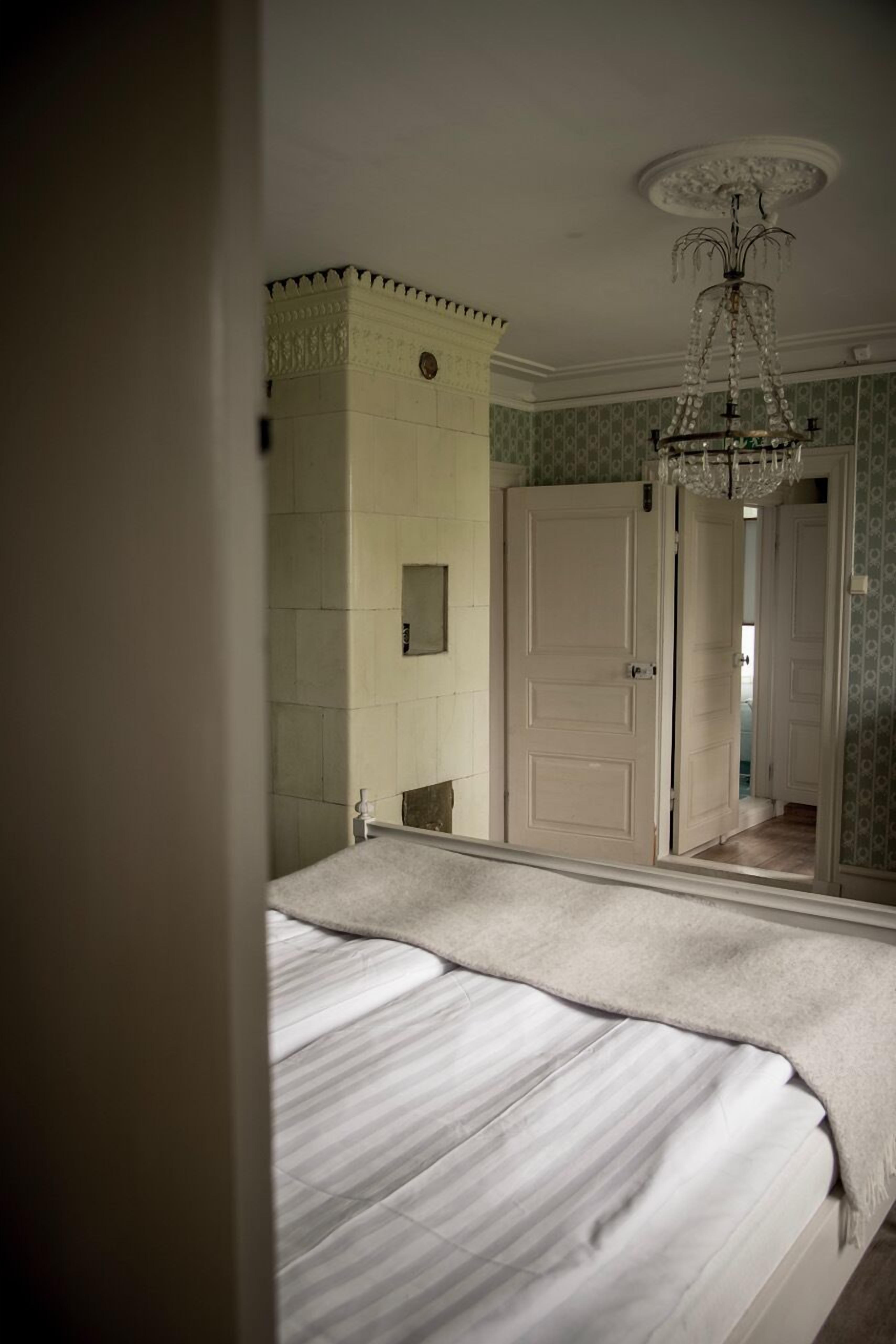 Une chambre à coucher avec un grand lit, un lustre, un miroir et une porte donnant sur une autre pièce.
