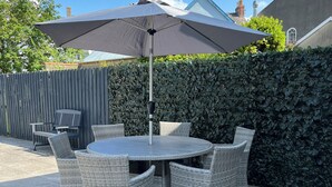 A round table with wicker chairs and a large umbrella, set on a patio with a hedge and a wooden fence in the background. - Castle cottage in the  town of Tenby 1 min walk  to the town 5 min walk to beach (Tenby)
