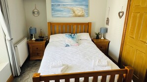 A bedroom with a wooden bed, a blue hanging lamp, a painting of a beach scene, and a wooden door. - Castle cottage in the  town of Tenby 1 min walk  to the town 5 min walk to beach (Tenby)