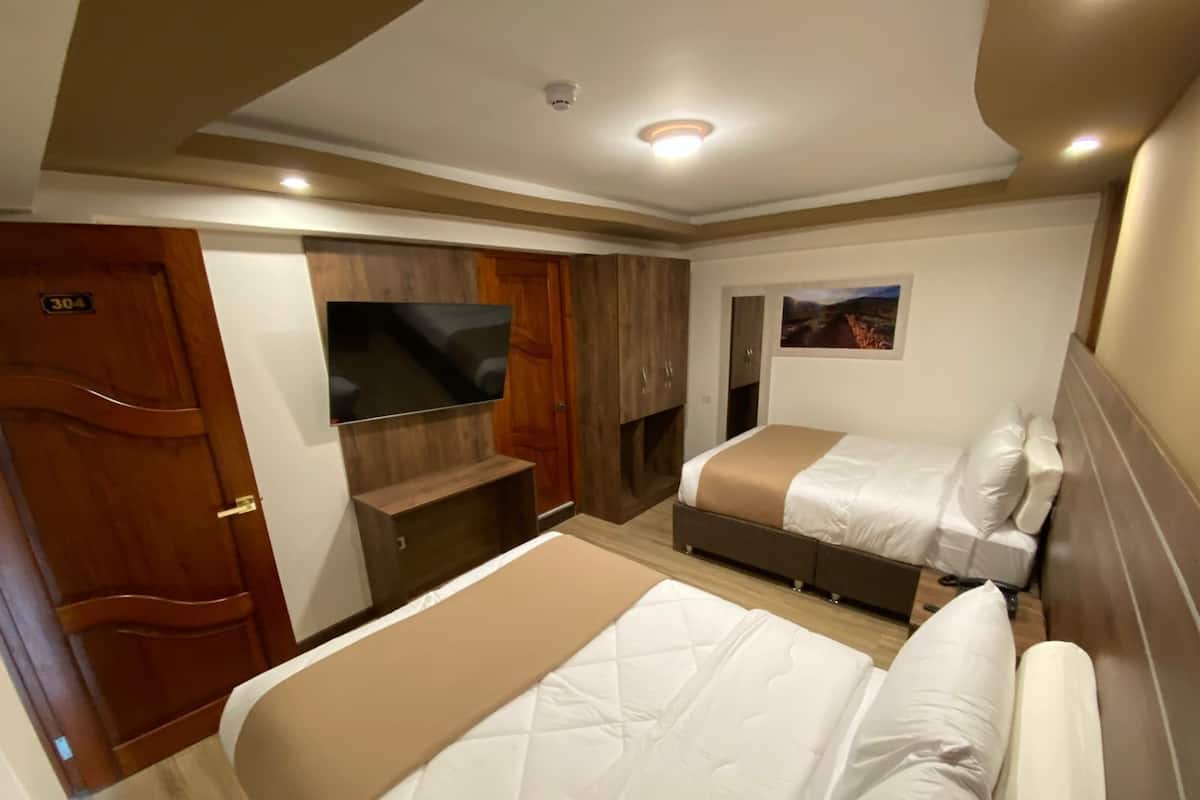 A hotel room with two beds, a TV, wooden cabinets, and a painting on the wall.