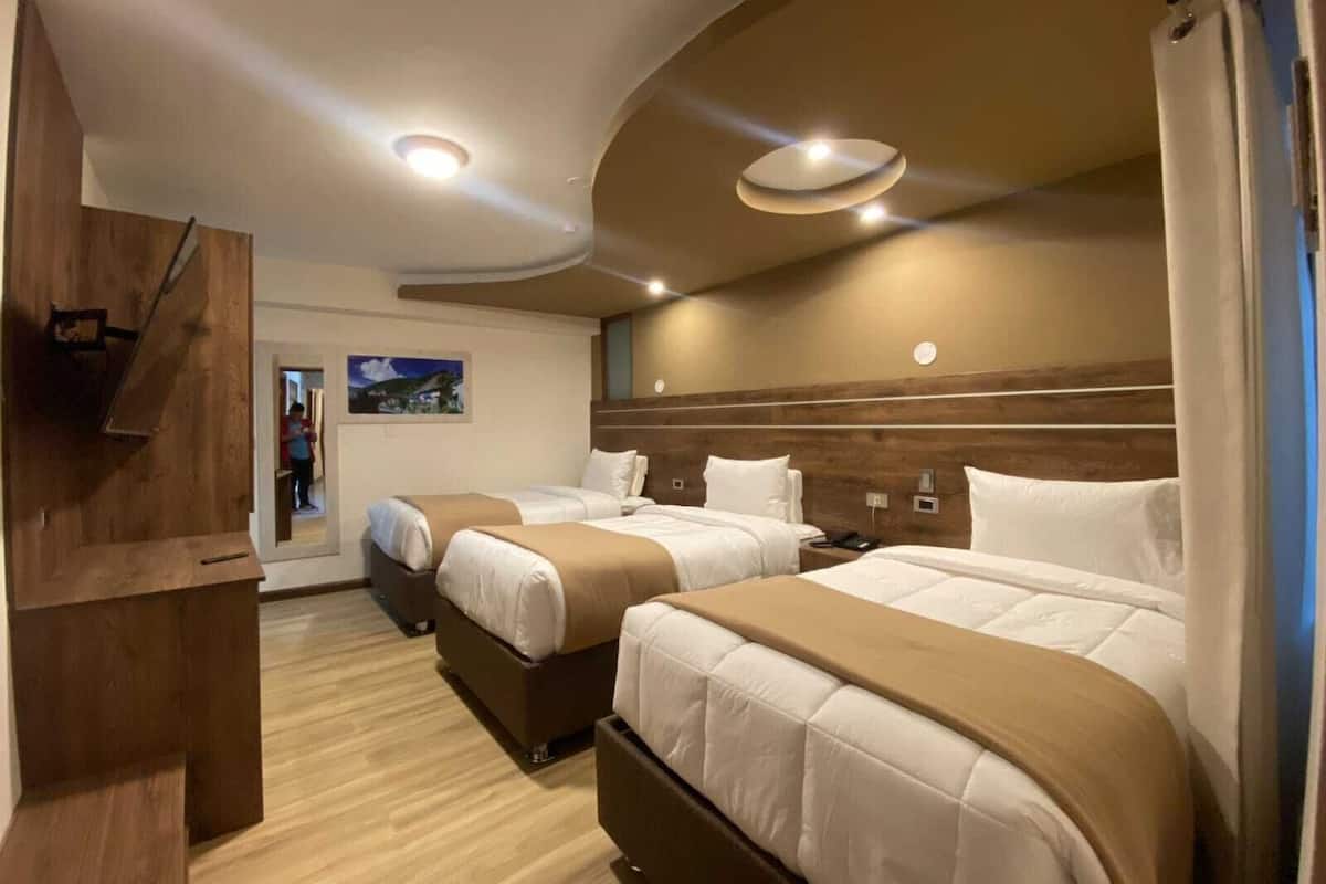 A hotel room with two beds, a wooden desk, and a painting on the wall.