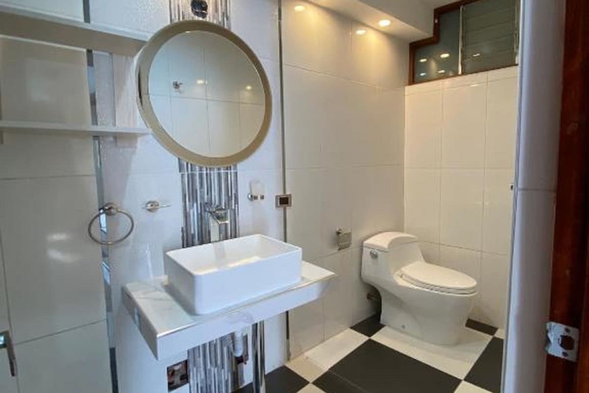 A modern bathroom with a white sink, mirror, and toilet. The floor has a black and white checkered pattern.