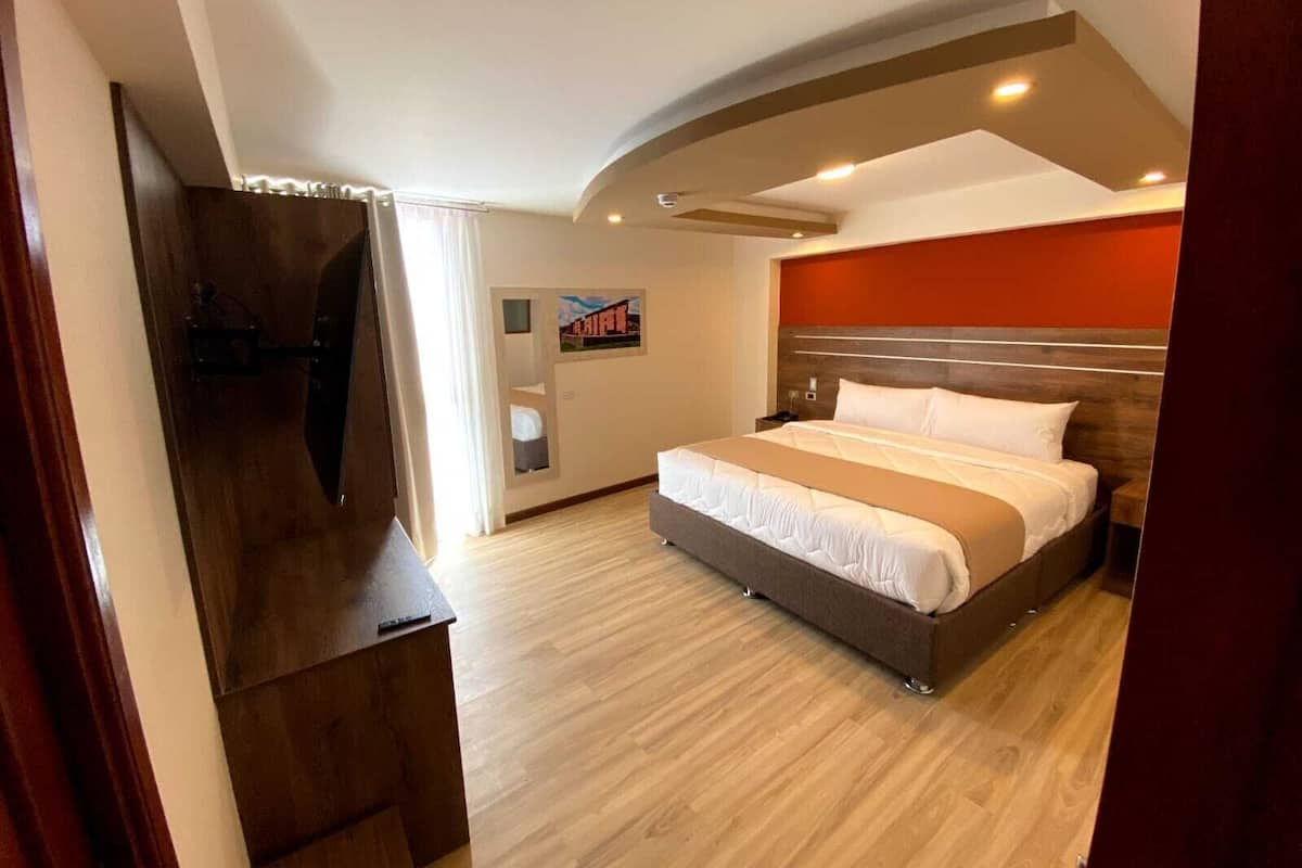 A hotel room with a large bed, a flat-screen TV, a wooden desk, and a red accent wall.