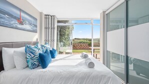 A modern hotel room with a large bed, white linens, blue patterned pillows, and a painting of sailboats on the wall.