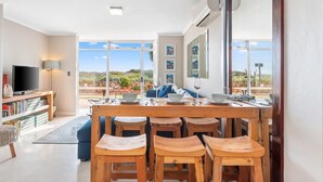 A modern living room with a wooden dining table, blue sofa, and wooden stools.