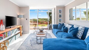 A modern living room with a blue sofa, a flat-screen TV, and a bookshelf.