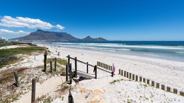 A beach with a wooden fence, sandy dunes, and a mountain in the background.