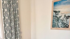 Una mesa de comedor blanca con cuatro sillas, una cortina estampada y un cuadro en la pared.