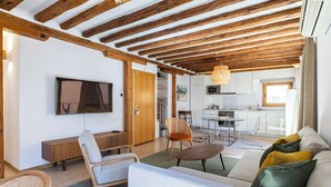 A modern living room with a wooden ceiling, a flat-screen TV, a sofa, a dining table, and a kitchen in the background. - Apartamento Luminos y Tranquilo Alado de la Plaza Mayor (Madrid)