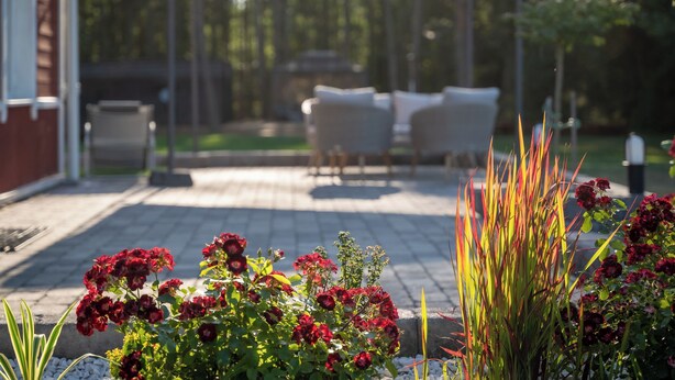 Un patio con mobiliario exterior, un espacio de estar techado y una diversidad de plantas.