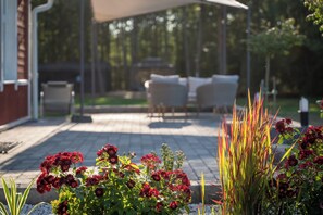 Un patio con mobiliario exterior, un espacio de estar techado y una diversidad de plantas.