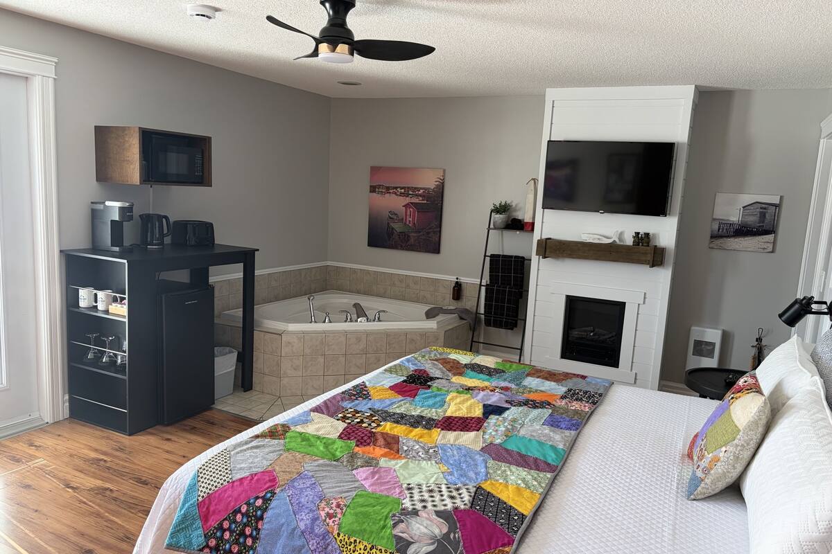 A bedroom with a bed, a bathroom with a bathtub, a ceiling fan, and a fireplace.
