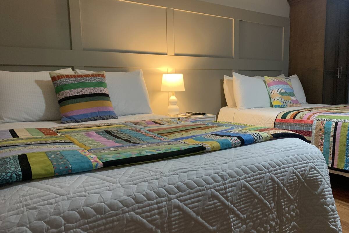 A hotel room with two beds, a nightstand with a lamp, and a headboard with built-in lighting.