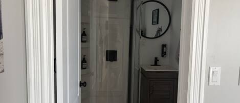 Un baño con cabina de ducha de vidrio, un mueble de madera, un lavabo y un espejo.