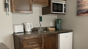 Une cuisine compacte dotée d’armoires en bois, d’un four à micro-ondes, d’une machine à café et d’un grille-pain.