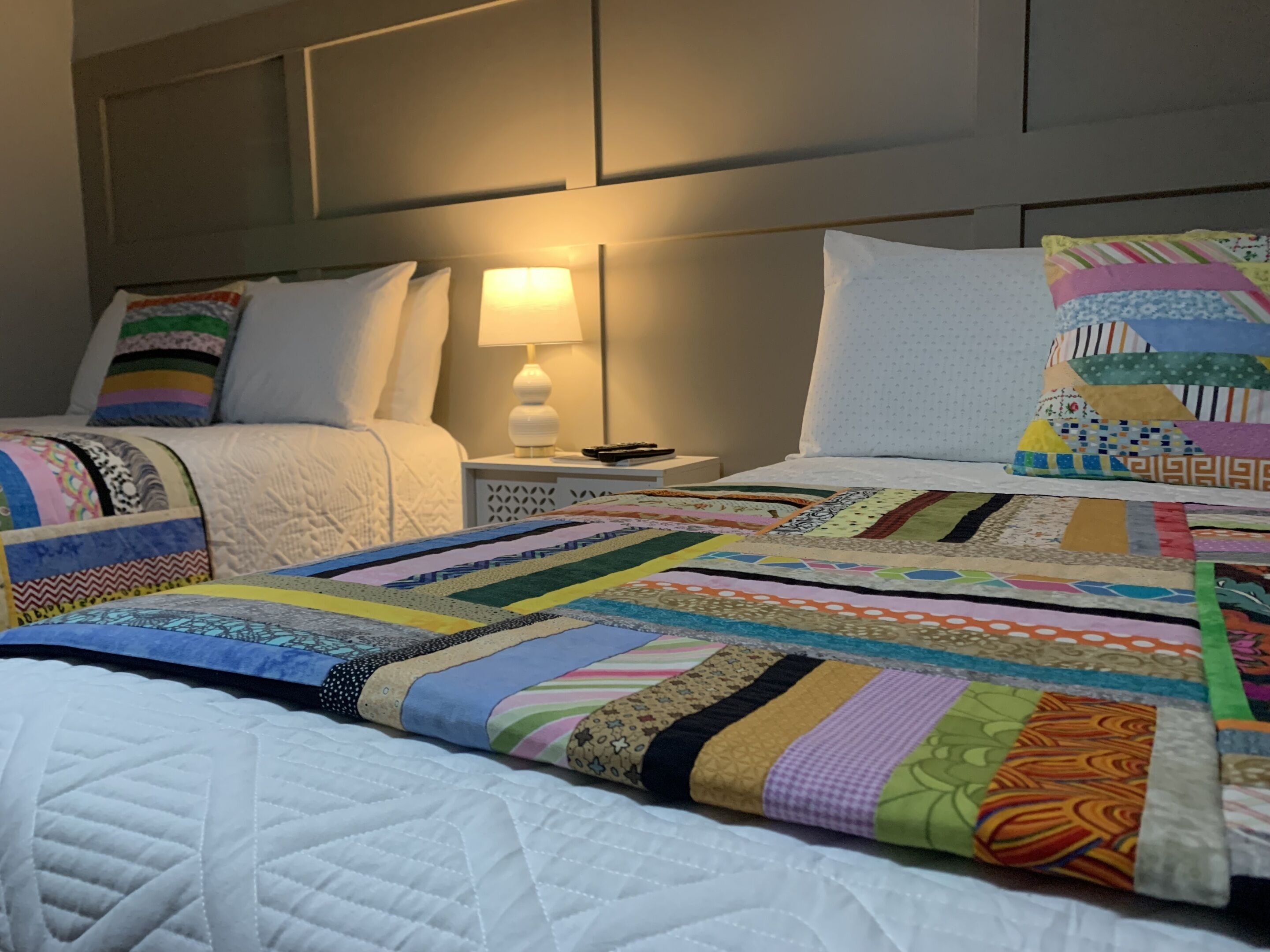 A hotel room with two beds, a nightstand with a lamp, and a headboard.