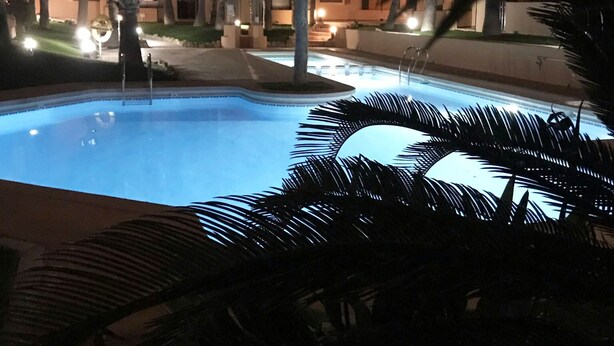 Une piscine entourée de palmiers et un bâtiment dont les fenêtres sont illuminées.