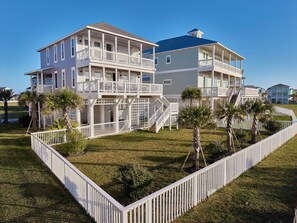 A multi-story beachfront property with balconies, a covered patio, and a fenced yard.