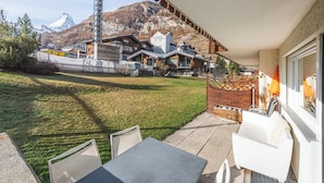 A patio with outdoor seating, a view of a mountain, and a building with a ski lift in the background. - 3,5 pièces, 4 à 6 personnes proche de la gare. (Zermatt)