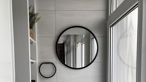 A modern bathroom with a wooden vanity, a black sink, a round mirror, and a window with frosted glass. - Moderner Tiny Bungalow am See in der Oberlausitz, zum Radfahren, Wandern, Angeln (Quitzdorf am See)