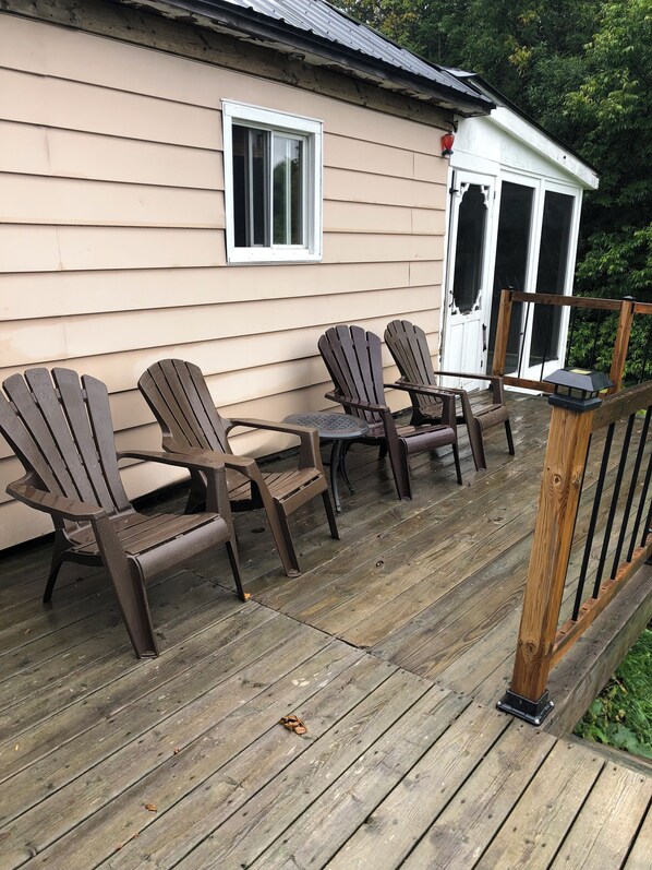 A deck with wooden chairs and a table, a small porch area, and a house with beige siding and a white door.