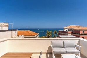 Μια βεράντα στην ταράτσα με θέα στη θάλασσα, ένας λευκός καναπές και ένα ξύλινο τραπέζι.