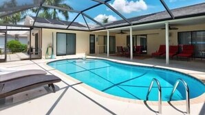 Ein Schwimmbecken mit Glasdach, umgeben von Liegestühlen und einer überdachten Terrasse.
