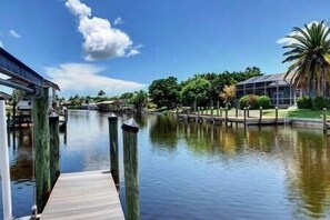 A calm waterway with a wooden dock extending into the water, surrounded by lush greenery and a clear blue sky.