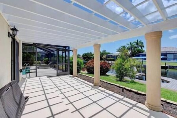 A covered outdoor area with a glass enclosure, columns, and a view of greenery and buildings.