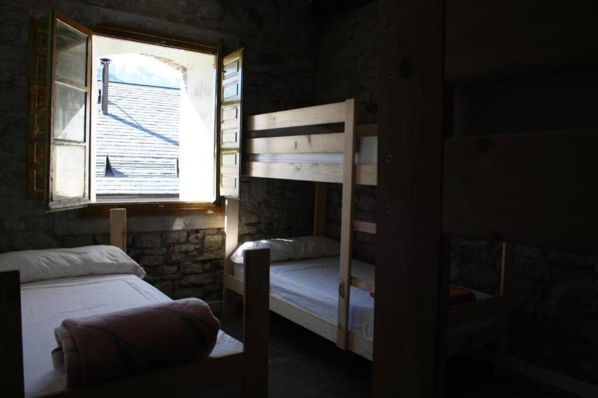 Quarto com beliches, parede de pedra e janela com persiana aberta.