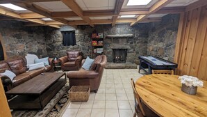 A cozy living room with a stone fireplace, leather sofas, a wooden coffee table, and a pool table.
