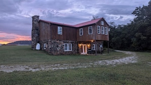 A rustic barn-style building with a stone foundation and wooden walls, featuring a red roof and a porch with outdoor seating.