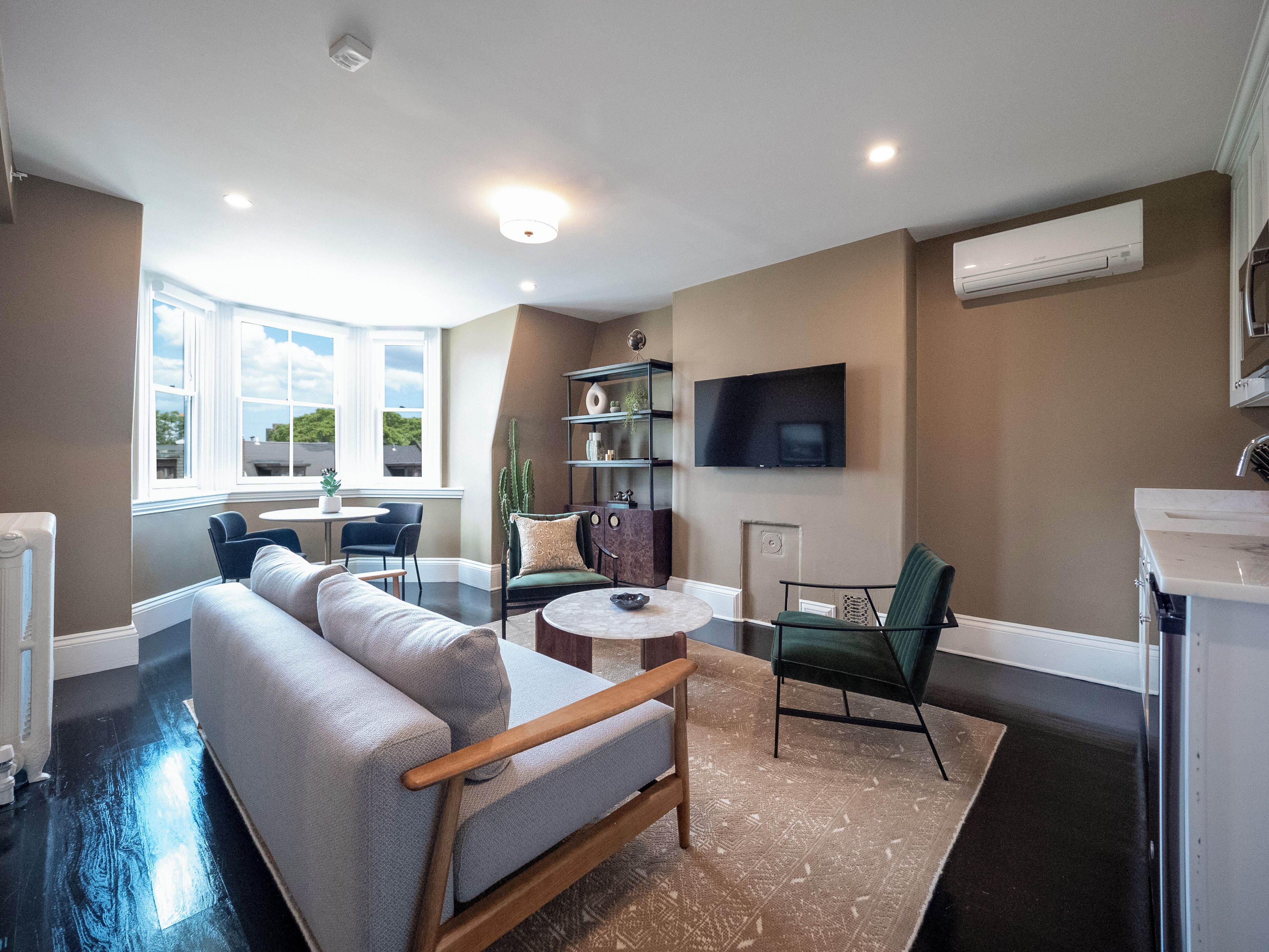 A modern living room with a sofa, chairs, a coffee table, and a TV. There is a window with a view of the outside.