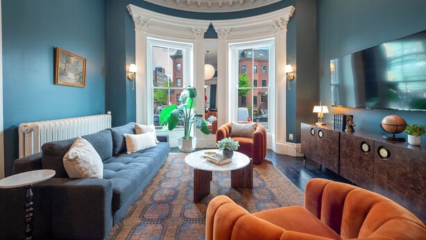 Un salon moderne avec un mur bleu, une grande fenêtre, un canapé, une table basse et un téléviseur.
