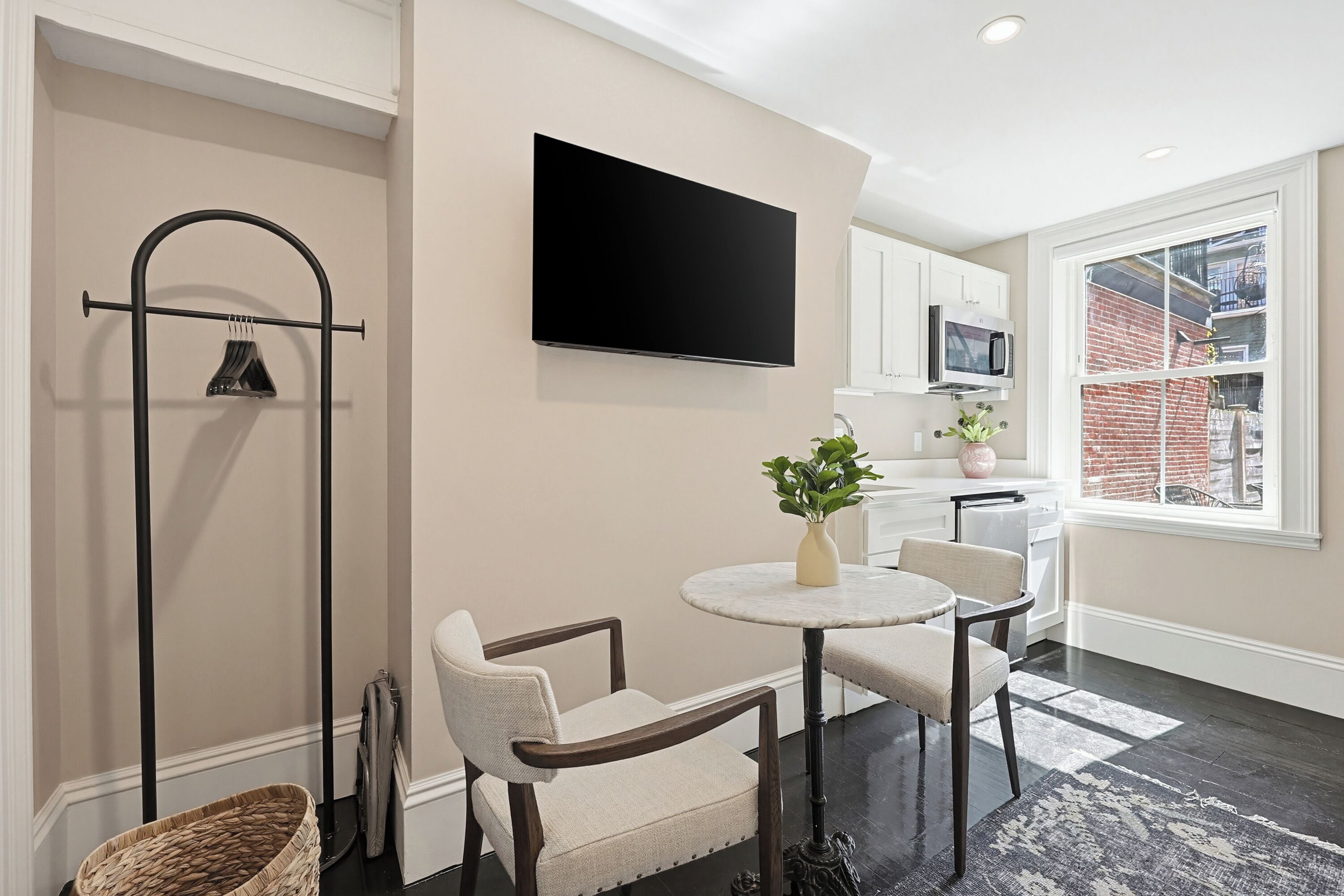 A modern kitchen with a flat-screen TV, a dining area with chairs, a small table, and a plant.