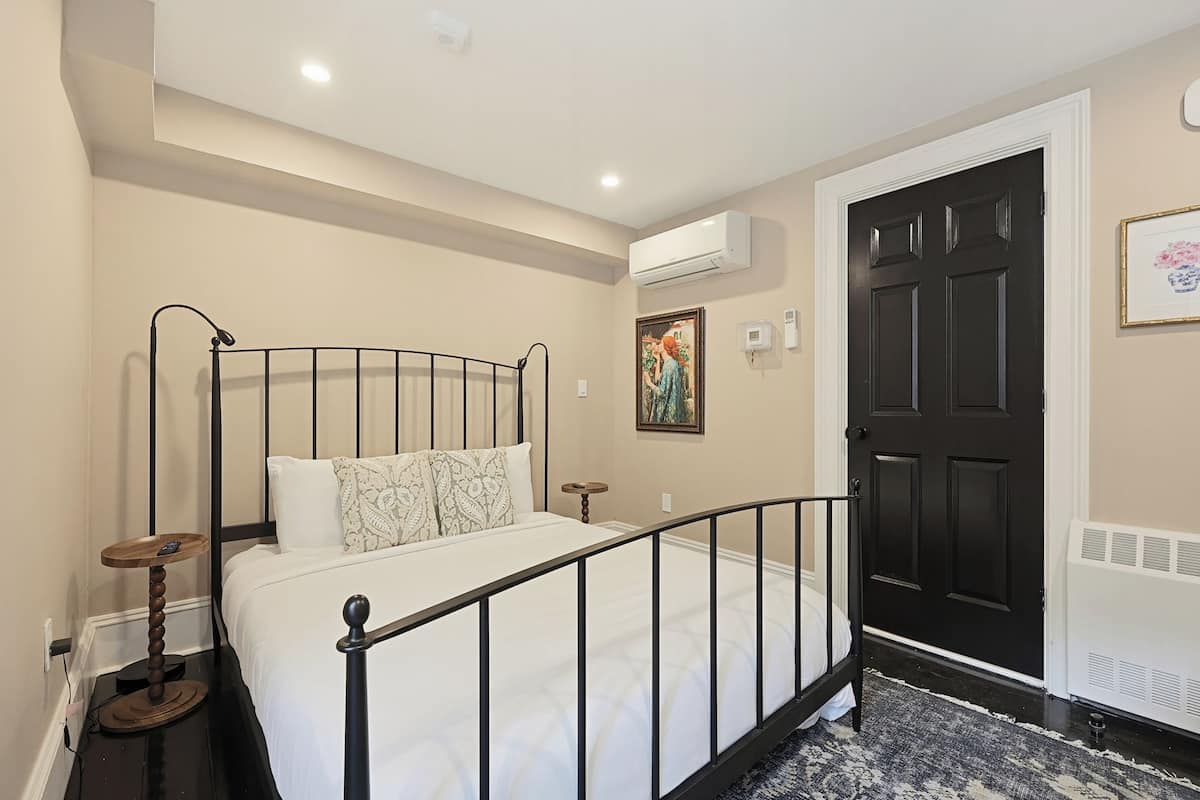 Un dormitorio con una cama, una mesita de noche, un aire acondicionado y un cuadro en la pared.