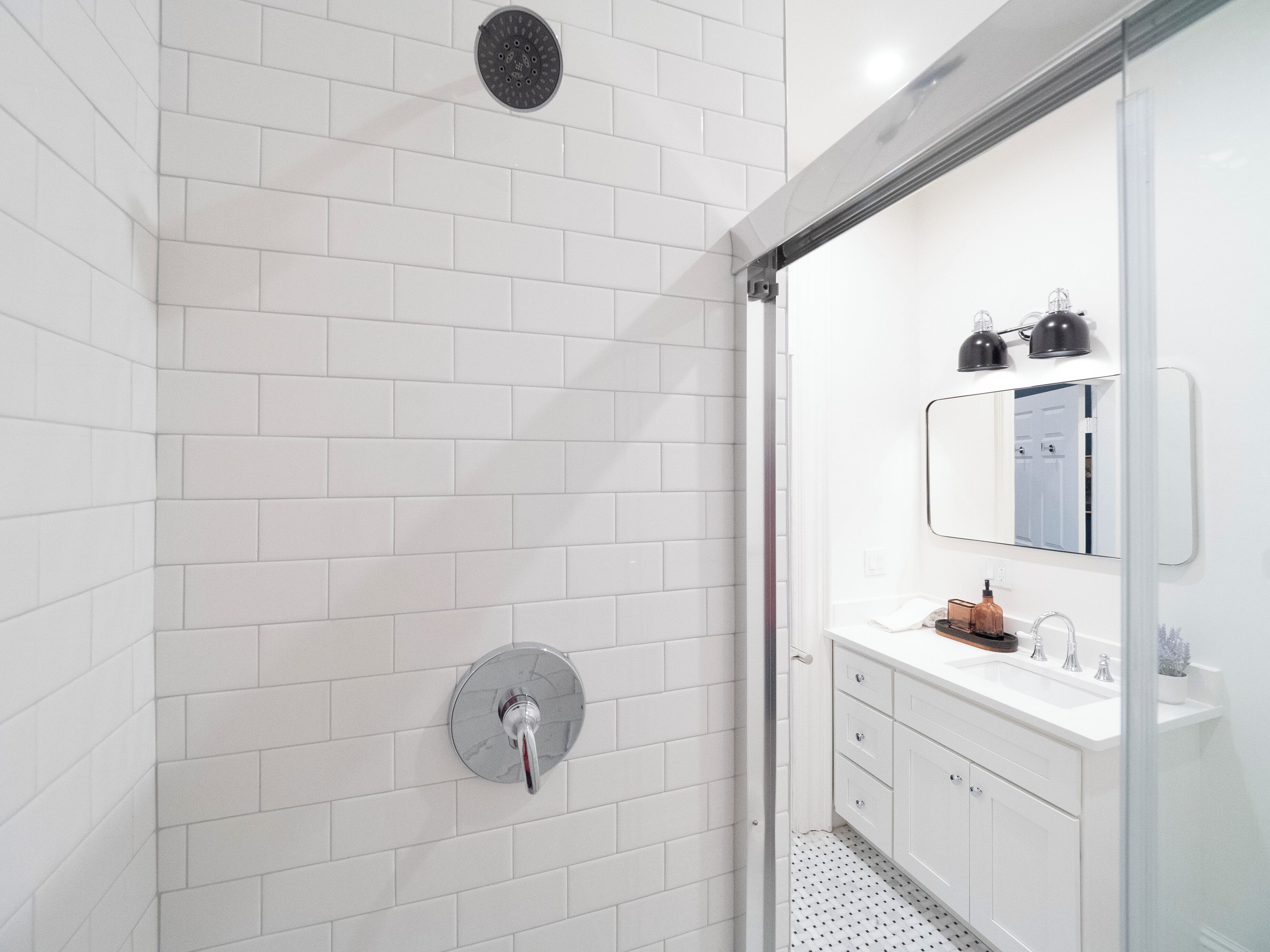 A modern bathroom with white subway tiles, a glass shower enclosure, a white vanity with a mirror, and a toilet.