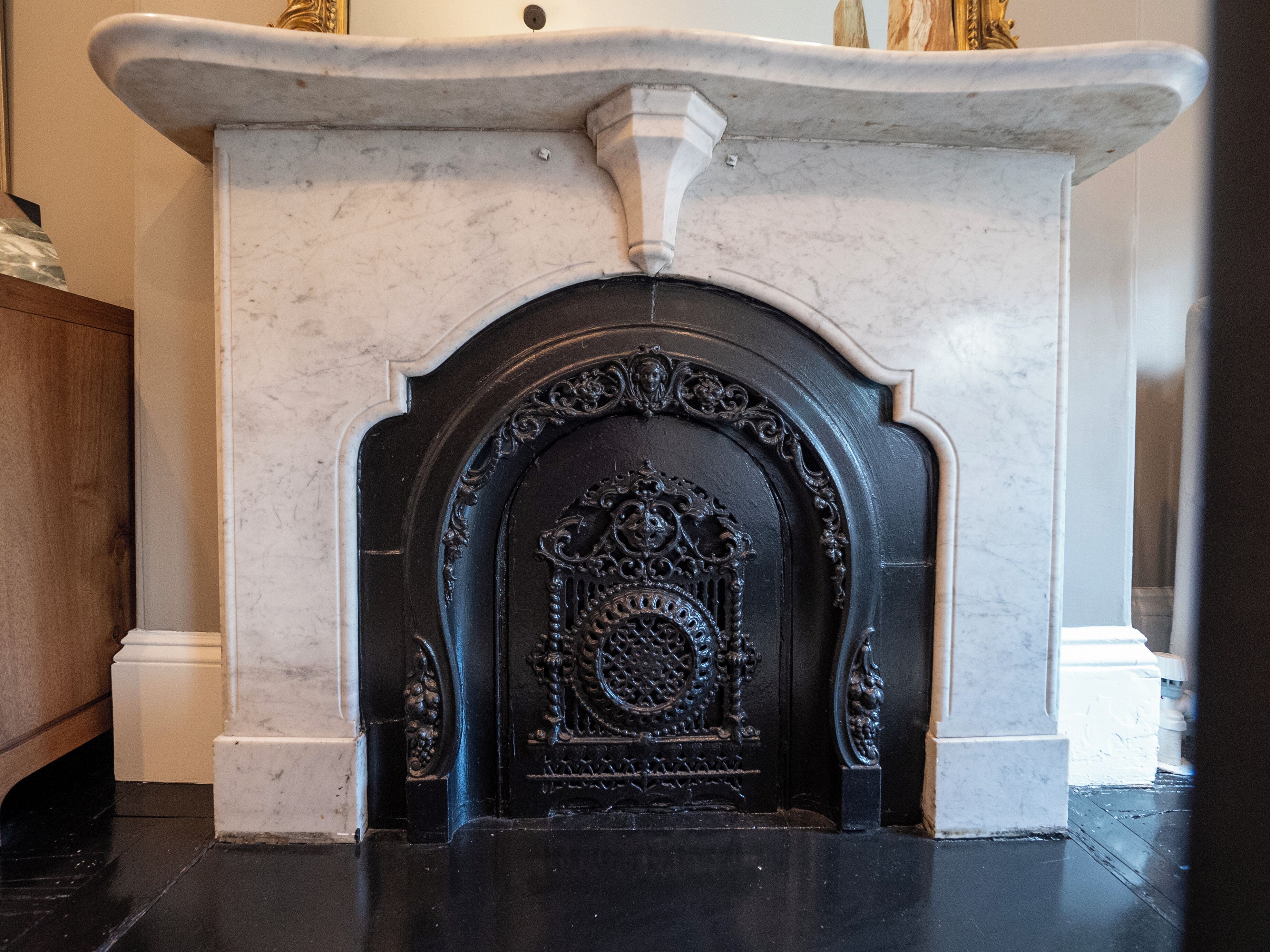 A marble fireplace with intricate carvings and a black surround.
