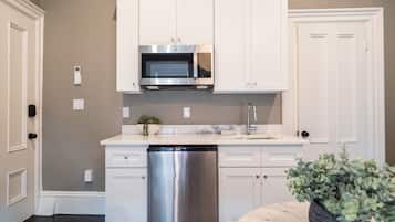 A kitchen with white cabinets, a stainless steel dishwasher, a microwave, and a sink.